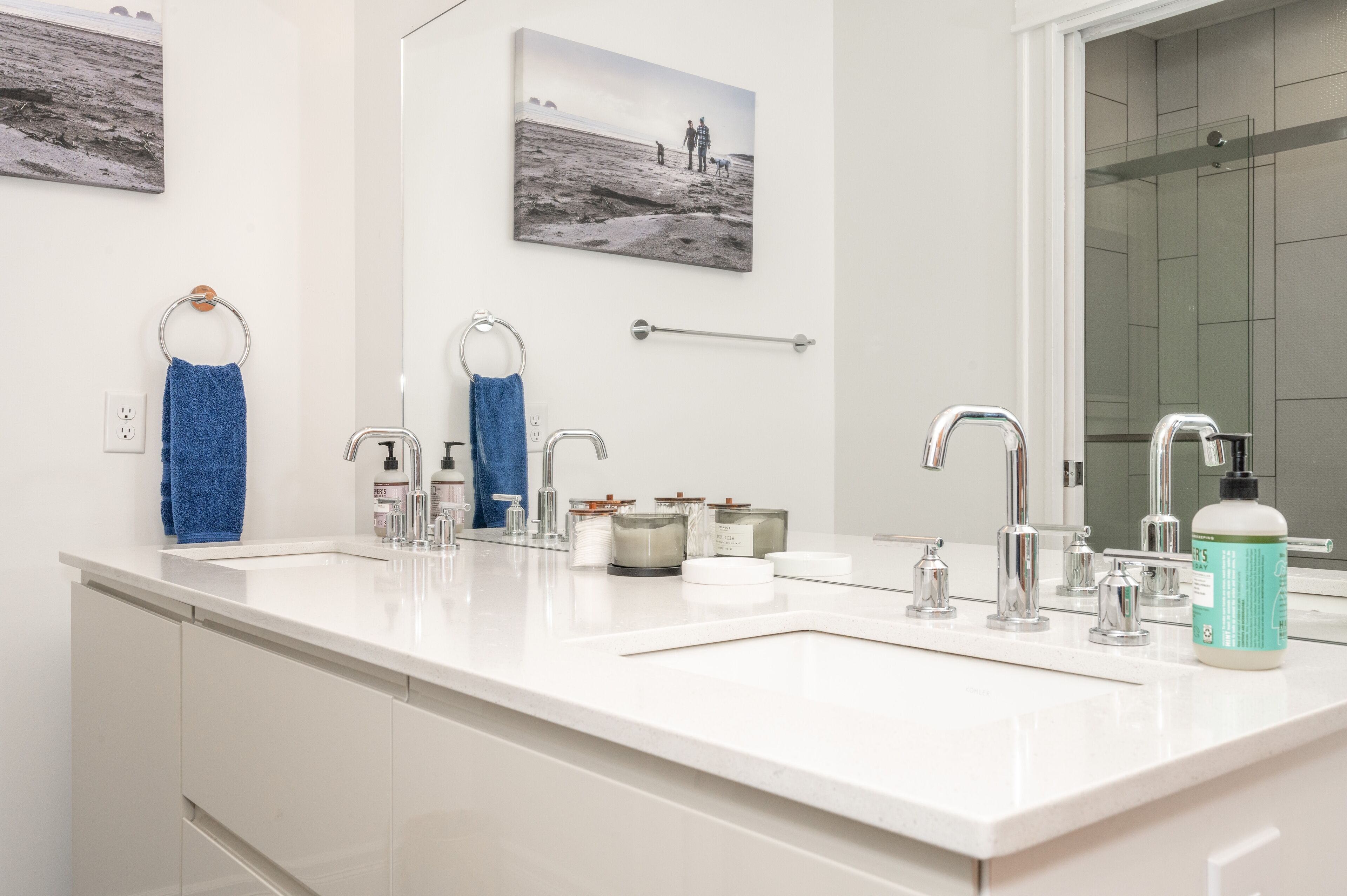 A modern bathroom with a white sink, two faucets, a large mirror, and a glass shower enclosure.