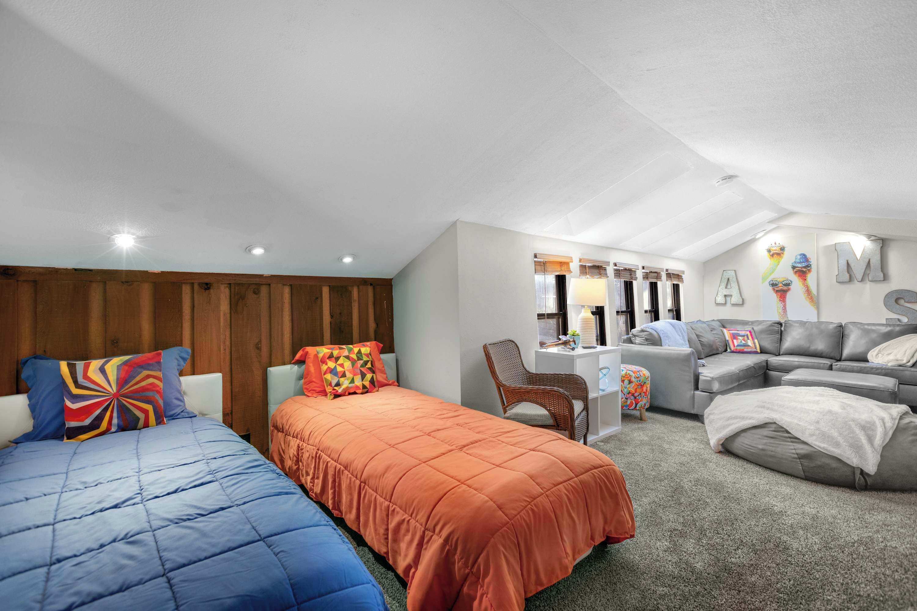 A bedroom with two beds, a desk, a sofa, and a wall with letters.