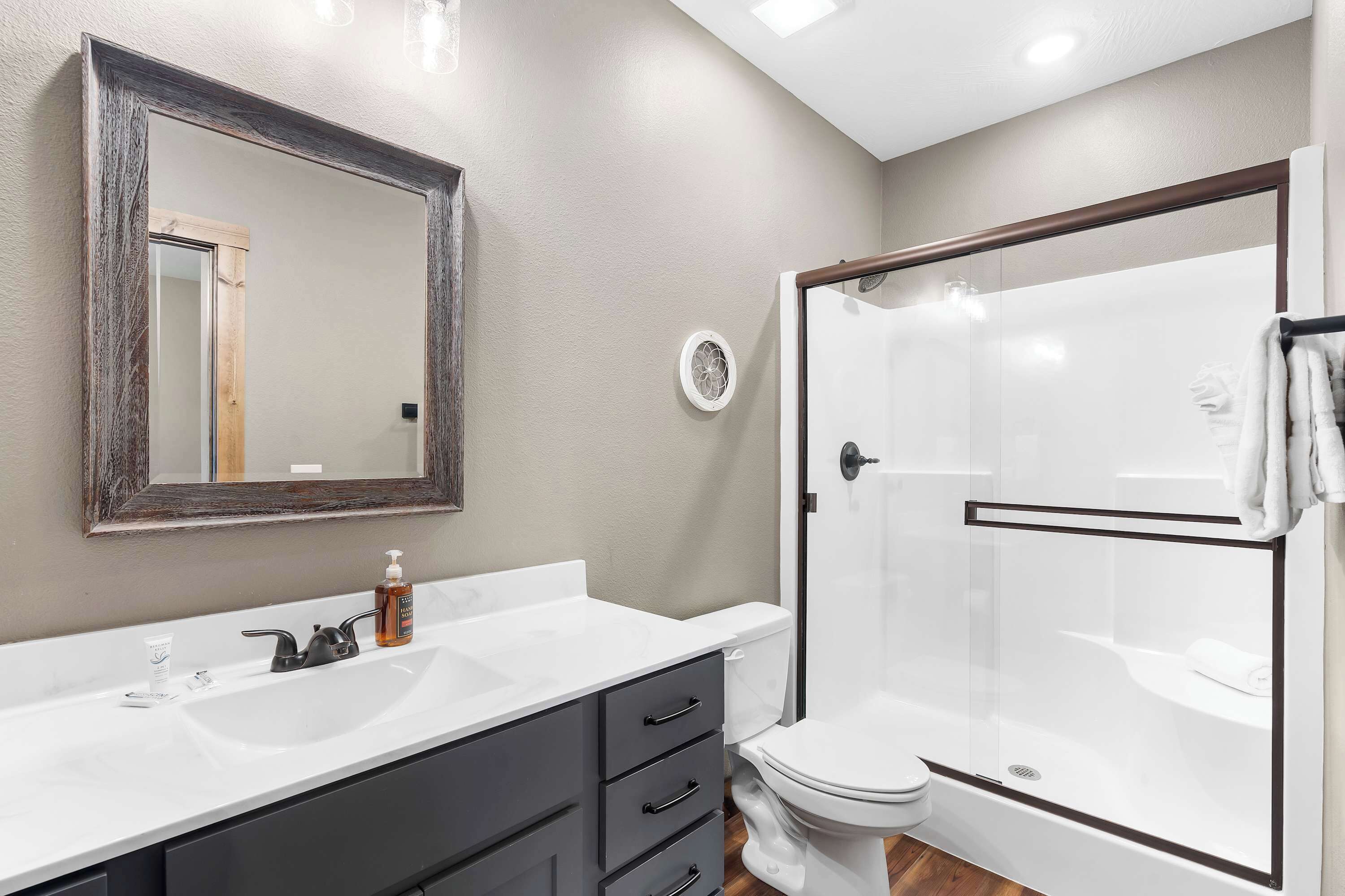 A bathroom with a white sink, dark gray cabinet, and a glass-enclosed shower.