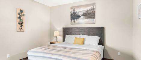 A bedroom with a bed, a nightstand with a lamp, a ceiling fan, and two wall art pieces.