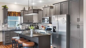 Een moderne keuken met grijze kastjes, roestvrijstalen apparatuur, een centraal eiland met krukken en een raam met uitzicht.
