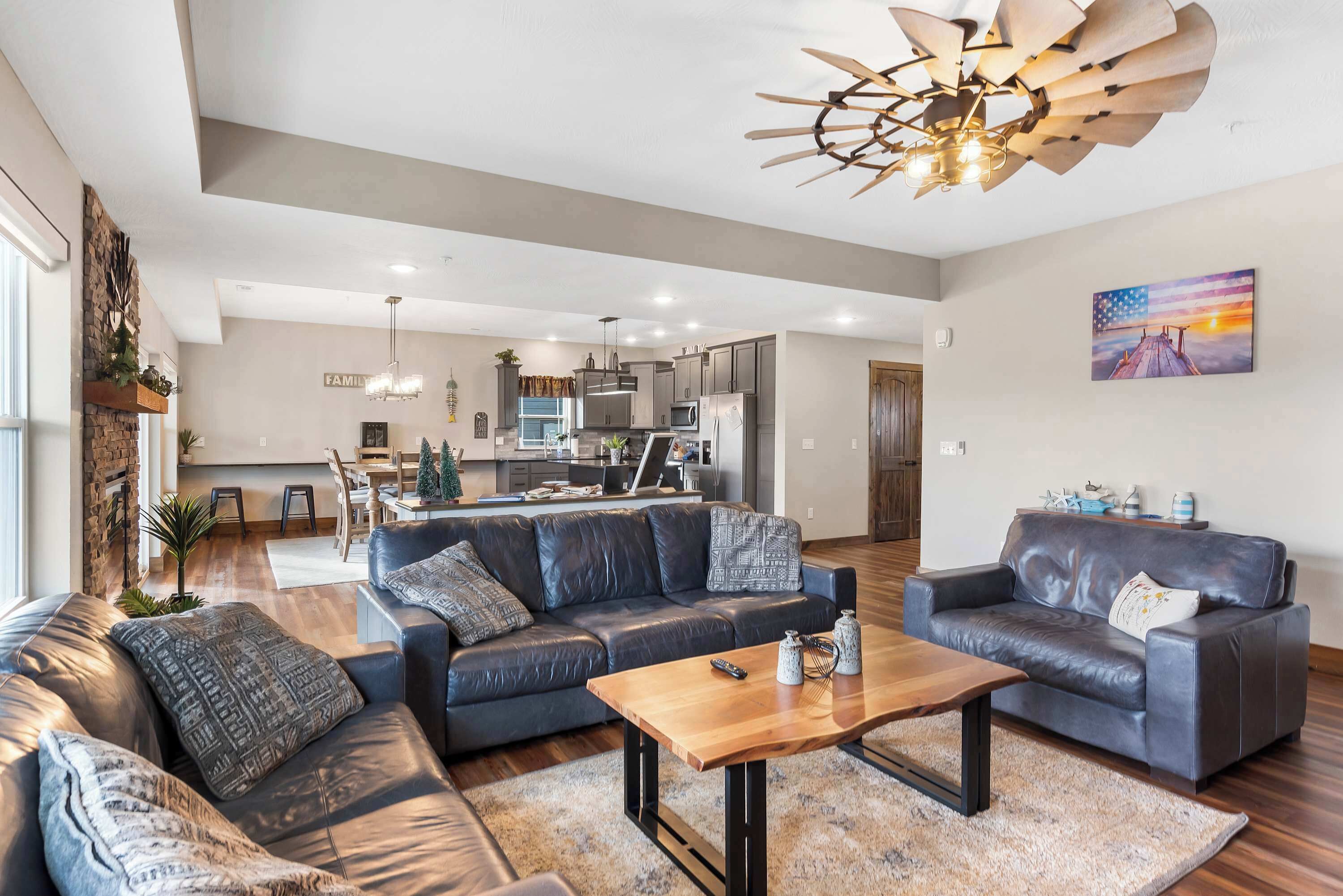 A spacious living room with a leather sofa, a wooden coffee table, and a modern ceiling fan.
