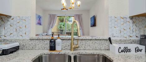 Una cocina con encimera de granito, pileta de acero inoxidable, grifo dorado y un letrero que dice "Coffee Bar".