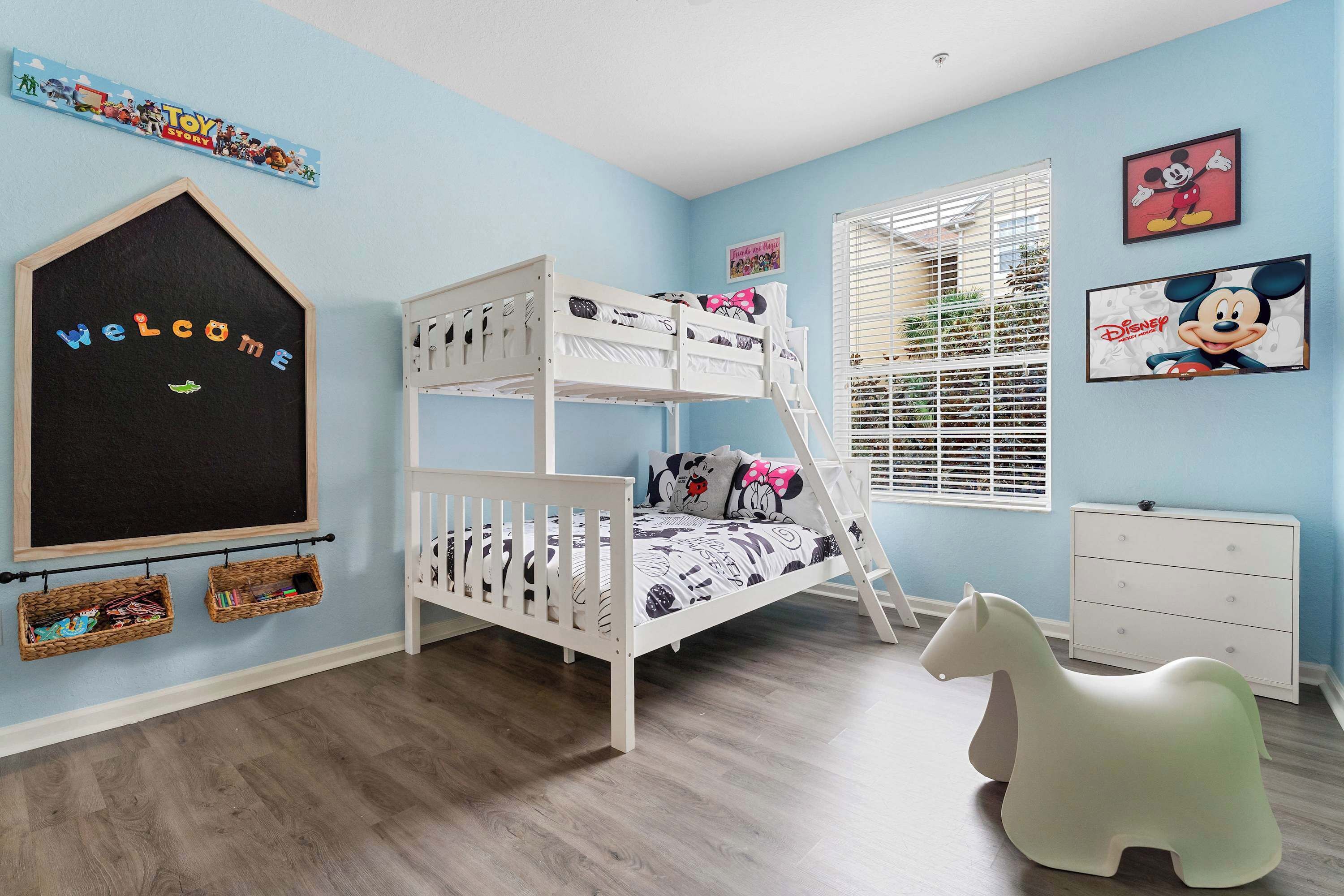 Een kinderkamer met een stapelbed, een witte ladekast, een speelgoedpaard en decoraties met Disney-thema.