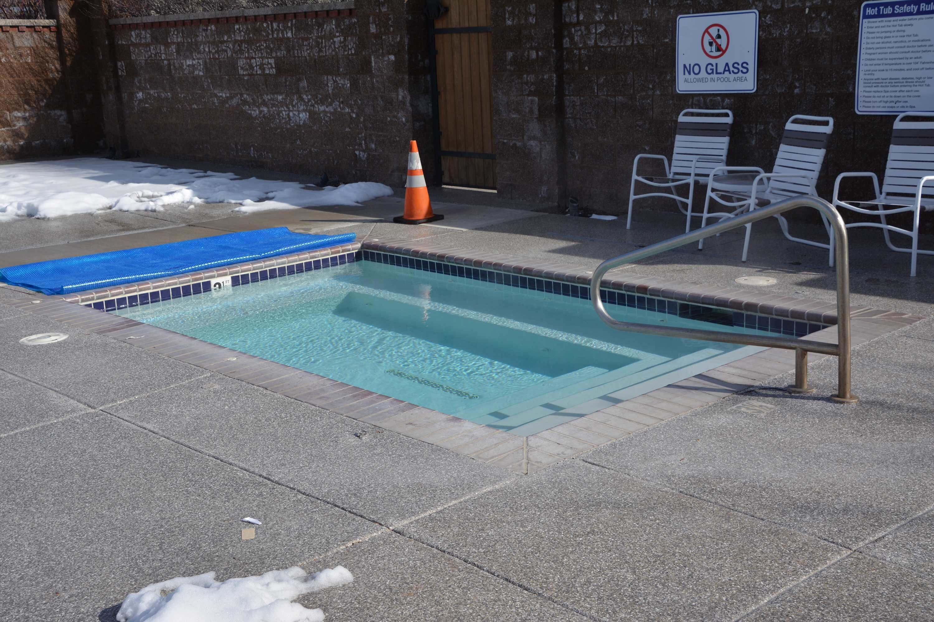 Une piscine avec un panneau indiquant qu'il est interdit d'y apporter des objets en verre, un tapis bleu et une échelle en métal.