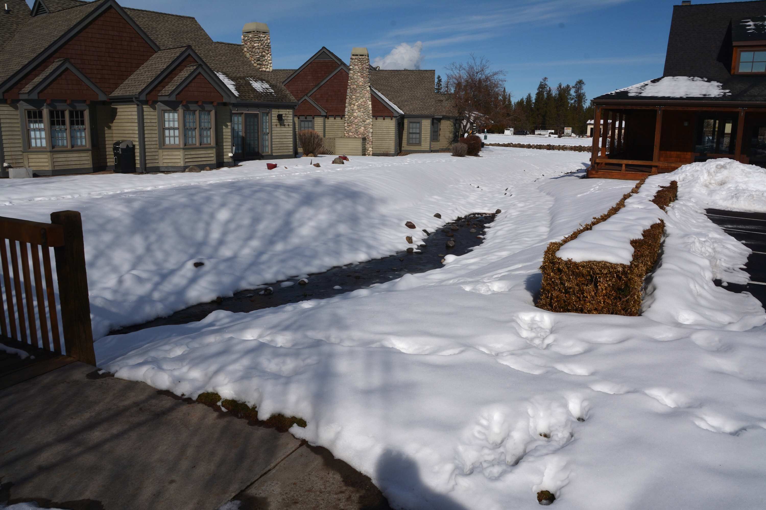 Un paysage enneigé avec un bâtiment en pierre, une terrasse en bois et un sentier recouvert de neige.