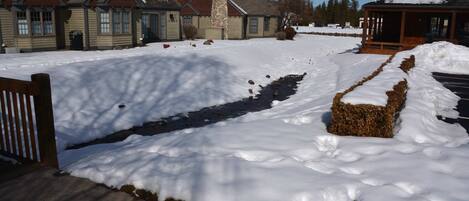 Un paysage enneigé avec un bâtiment en pierre, une terrasse en bois et un sentier recouvert de neige.
