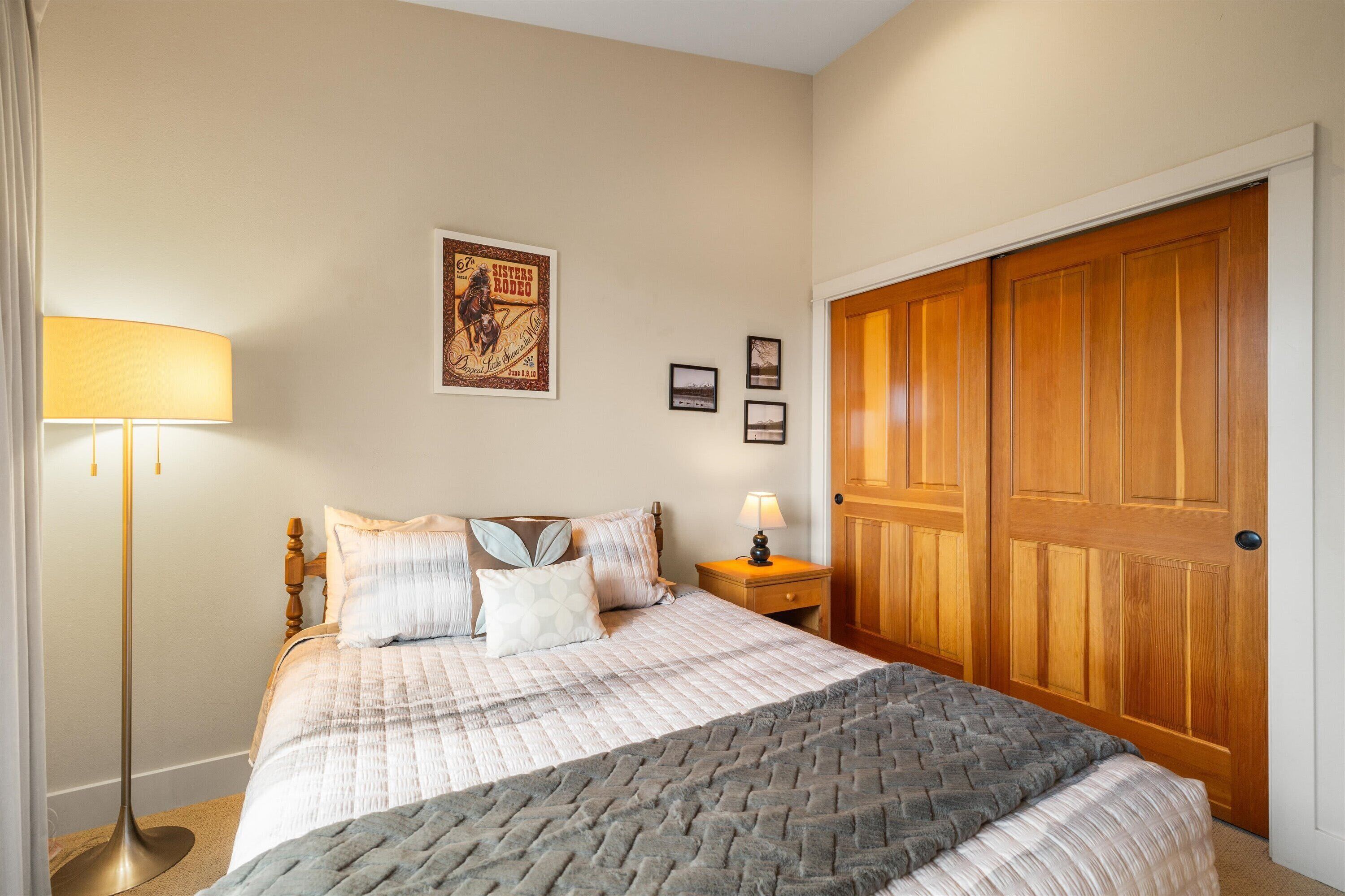 Un dormitorio con una cama, una mesita de noche con lámpara, un armario de madera y un cartel en la pared.