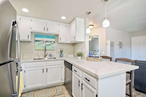 Una cocina moderna con armarios blancos, un refrigerador de acero inoxidable, lavavajillas y encimera de mármol.