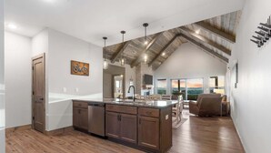 A spacious kitchen with a large island, wooden beams on the ceiling, and a view to the living area. - Two Pines Endless Views and Attractions! (Branson)