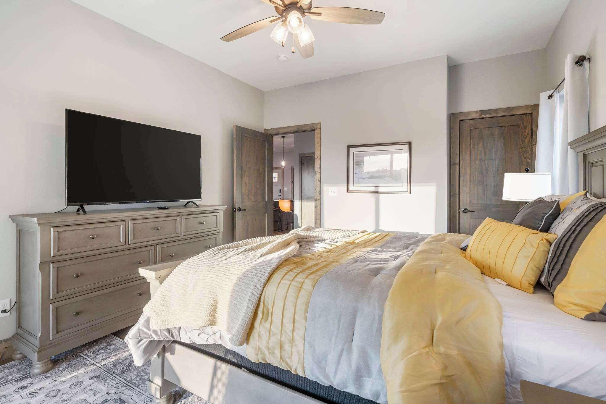 A bedroom with a bed, a dresser, a television, and a ceiling fan.