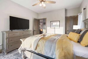 A bedroom with a bed, a dresser, a television, and a ceiling fan.