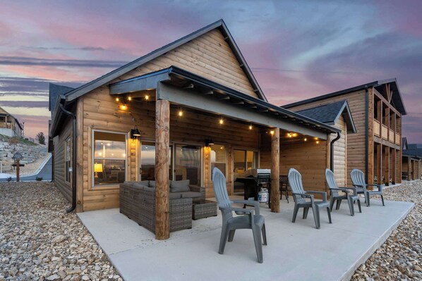 A wooden cabin with a covered patio, outdoor seating, and a grill area.
