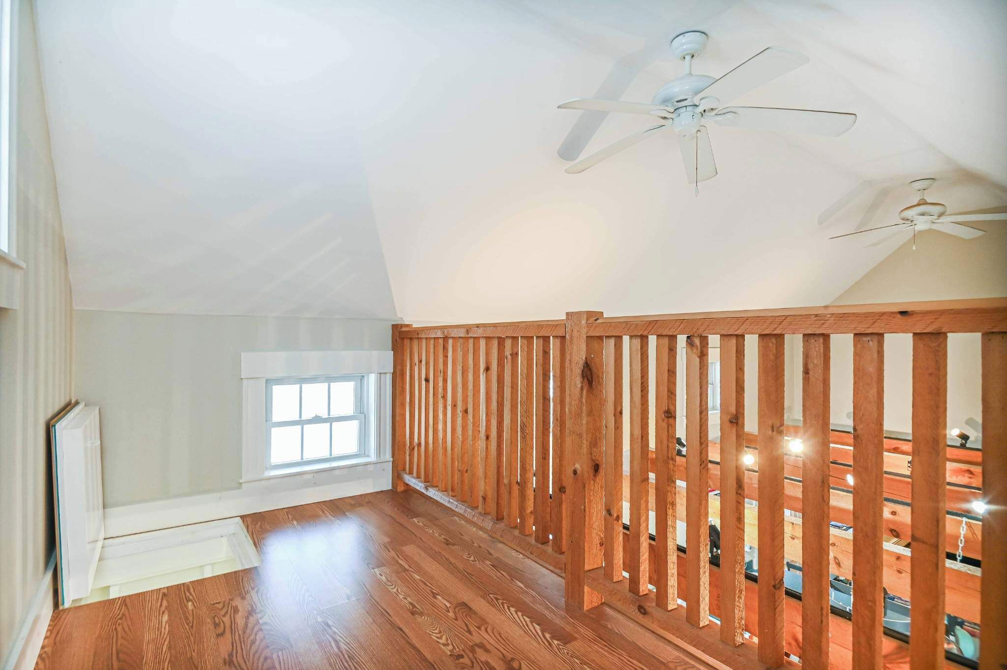 A spacious room with wooden flooring, a sloped ceiling with two ceiling fans, a large window, and a view of a boat dock.
