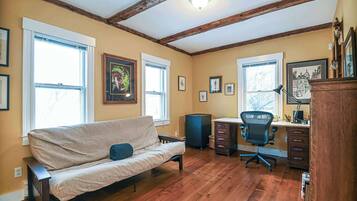 A room with a wooden floor, a sofa, a desk with a chair, and framed pictures on the walls.