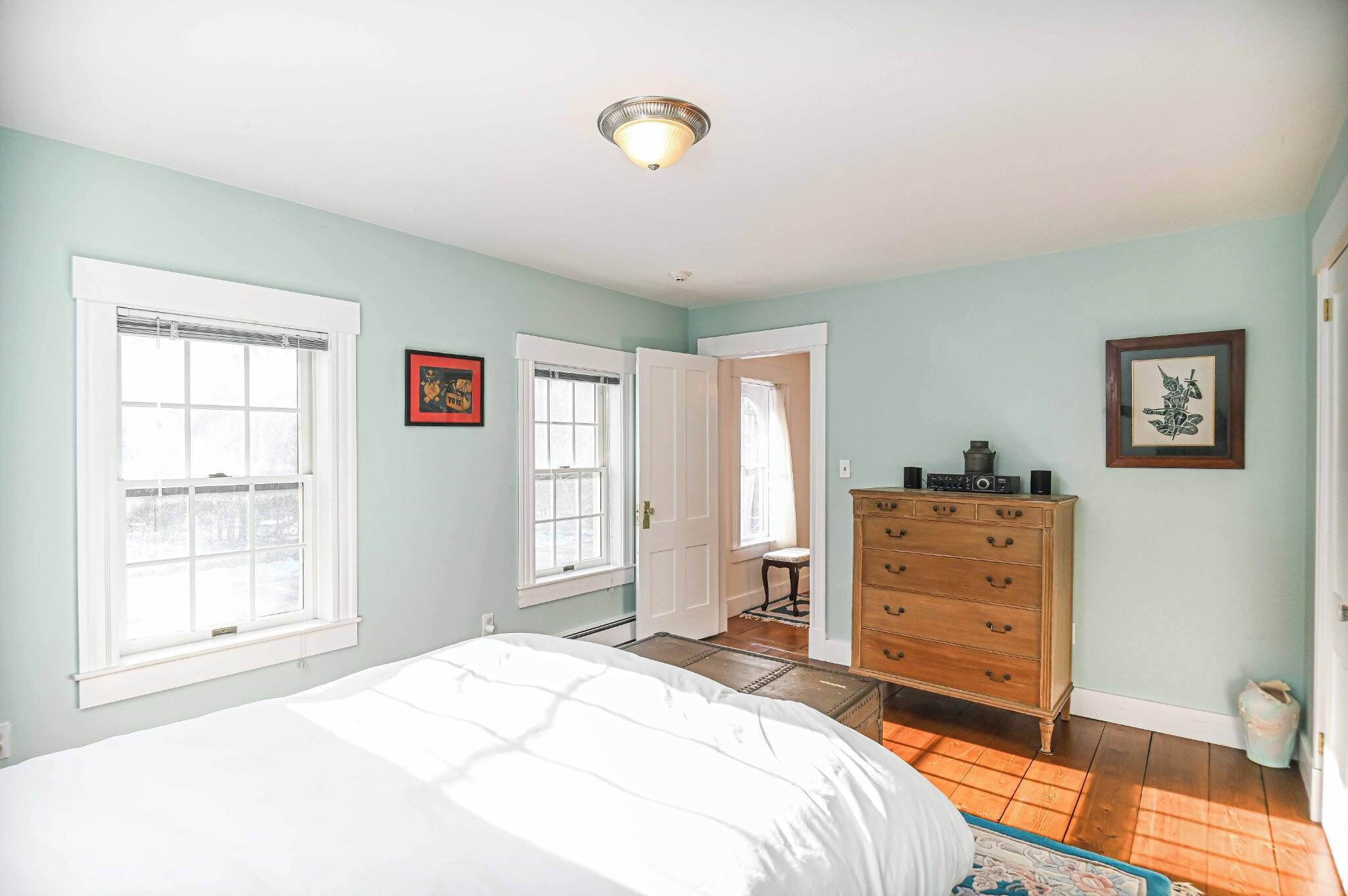 A bedroom with a bed, dresser, and two windows.