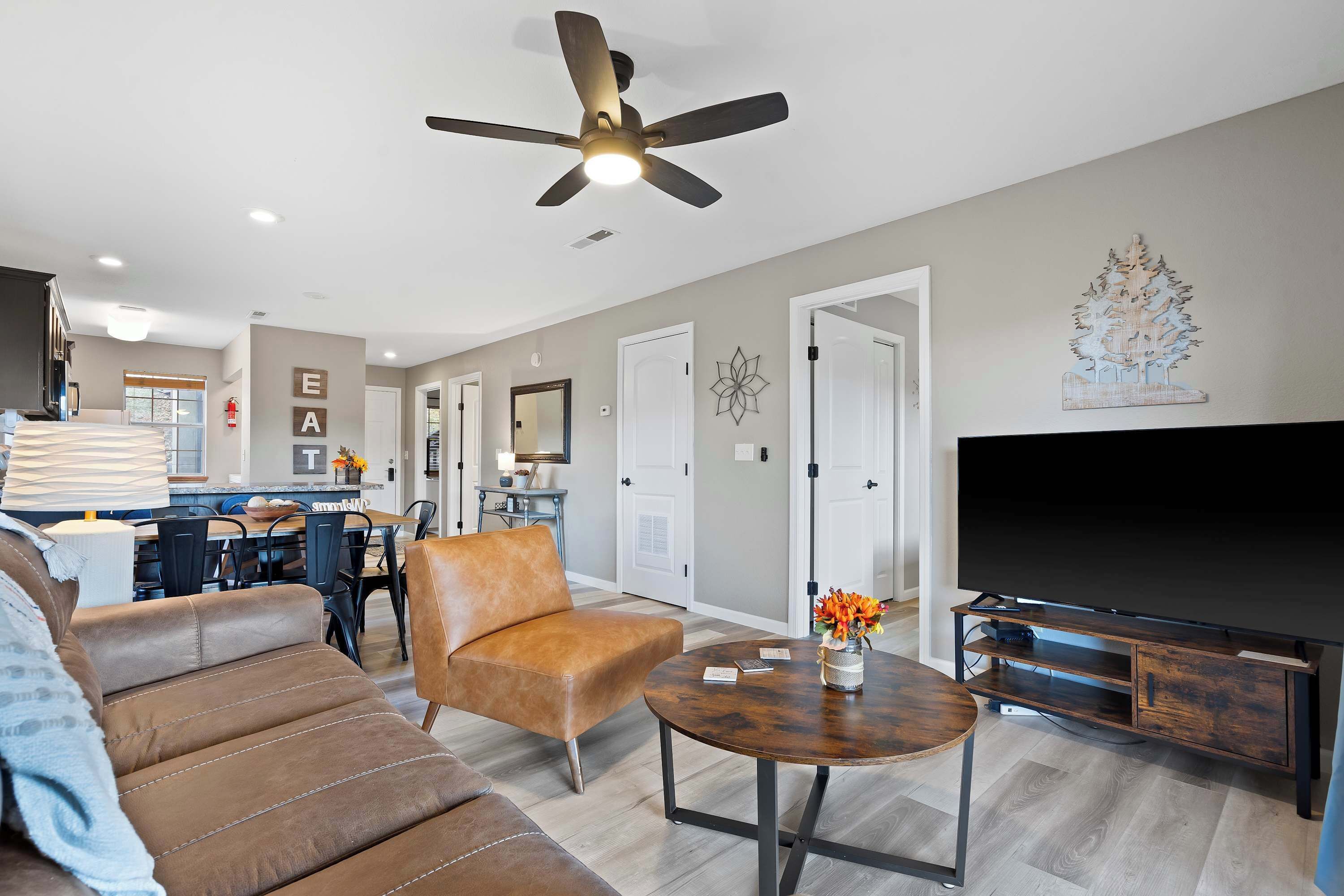 A modern living room with a sofa, armchair, coffee table, TV stand, and ceiling fan.
