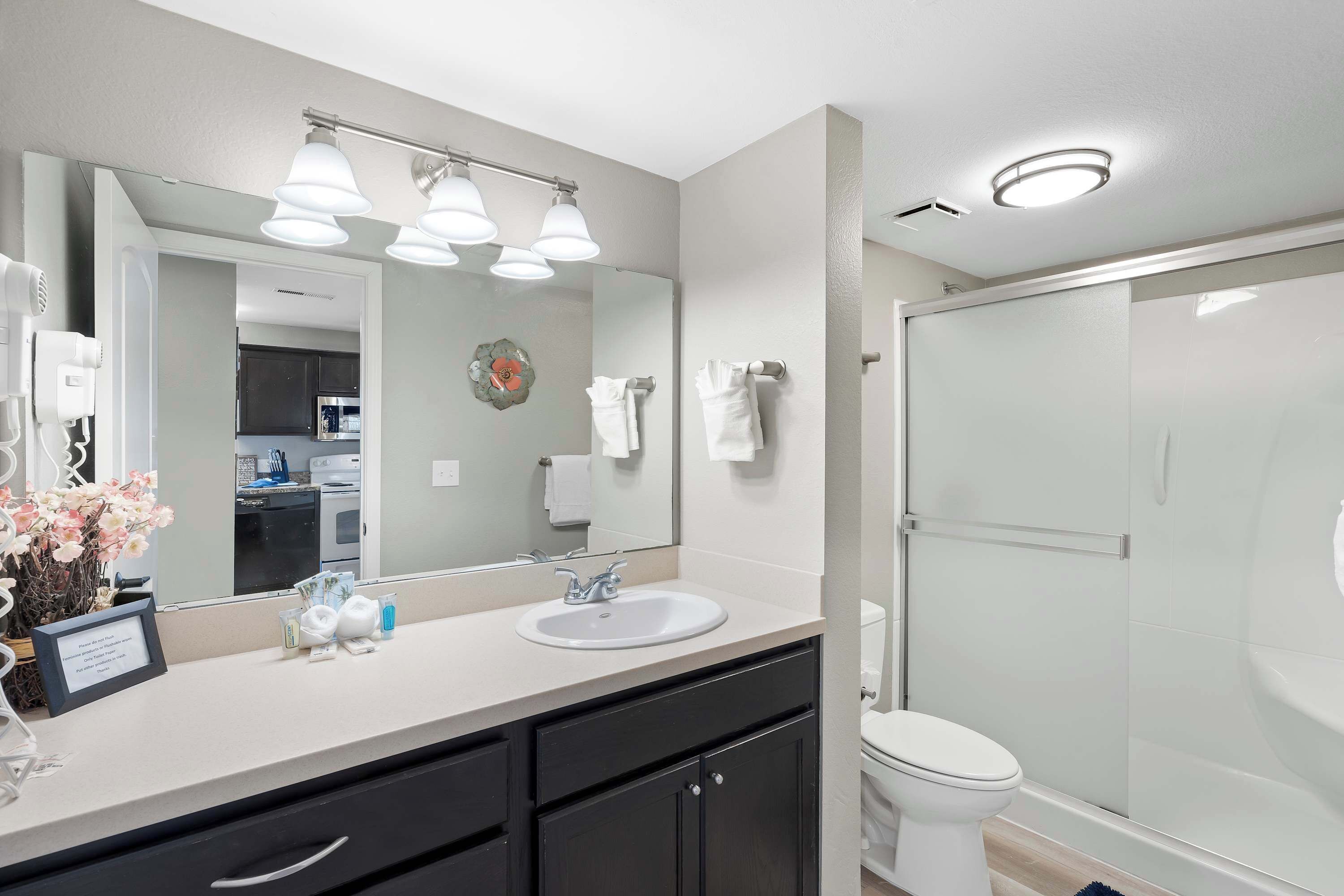 A modern bathroom with a large mirror, a sink, and a toilet. There is a shower area with a glass door.
