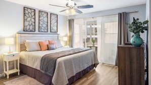 A bedroom with a bed, bedside tables, a ceiling fan, artwork on the wall, and a view through the window. - Brookside Haven - Gorgeous, Private Community! (Branson)