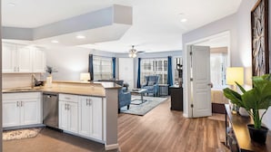 A modern kitchen with white cabinets, a wooden countertop, and a dishwasher. There is a dining area with a blue chair and a small table. - Brookside Haven - Gorgeous, Private Community! (Branson)