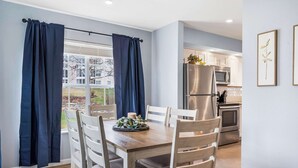 A dining area with a wooden table and chairs, a view of the kitchen, and a window with curtains. - Brookside Haven - Gorgeous, Private Community! (Branson)