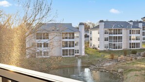 A residential building with multiple floors, large windows, and a small pond in the foreground.