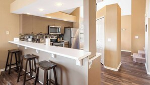 A modern kitchen with a white countertop, dark stools, and stainless steel appliances.