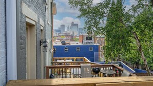 En balkon med udendørs siddepladser med udsigt over et bybillede med bygninger og et træ.