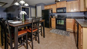 A modern kitchen with wooden cabinets, a black refrigerator, a microwave, an oven, and a dining table with chairs. - Birdie's Bliss 2BR Condo Sleeps 6! (Lake Ozark)