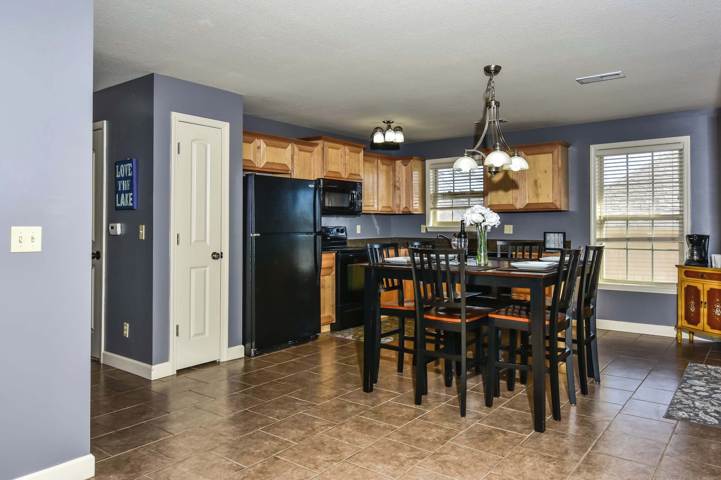 A kitchen with wooden cabinets, a black refrigerator, a dining table with chairs, and a chandelier.