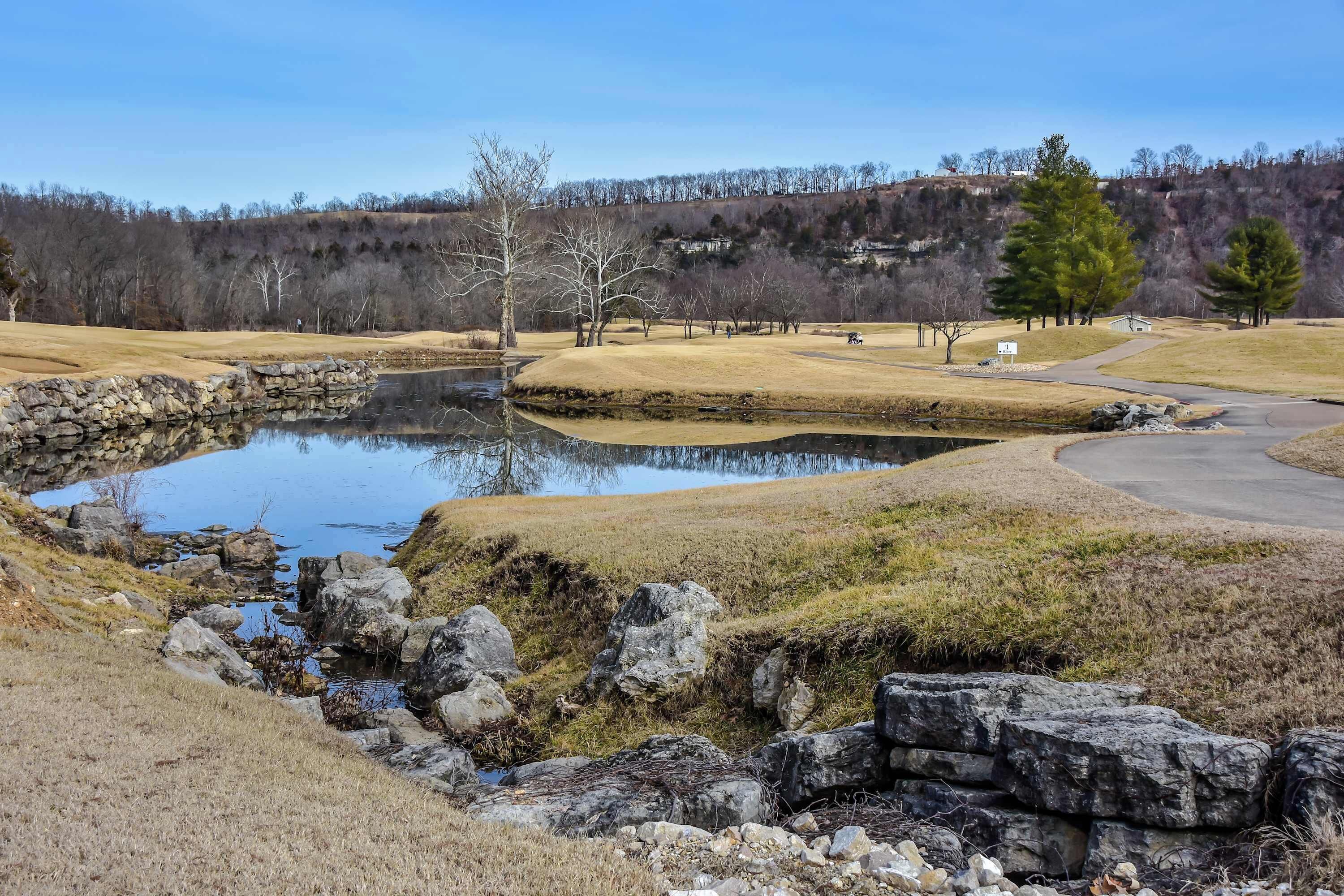 A tranquil golf course with a pond, stone walls, and a clear sky.