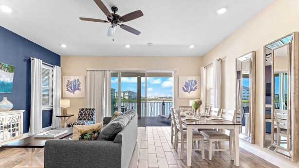 A spacious living room with a grey sofa, a dining table with chairs, and a ceiling fan. - Lafitte's Landing Lakeview Cottage - Lakefront! (Kissimmee)