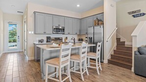 A modern kitchen with grey cabinets, a central island with bar stools, a microwave, and a refrigerator. - Lafitte's Landing Lakeview Cottage - Lakefront! (Kissimmee)