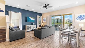 A modern living room with a sofa, a dining table set for four, and a ceiling fan. - Lafitte's Landing Lakeview Cottage - Lakefront! (Kissimmee)