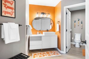 Ein modernes Badezimmer mit einem weißen Waschtisch, einem runden Spiegel und einer orangefarbenen Wand.