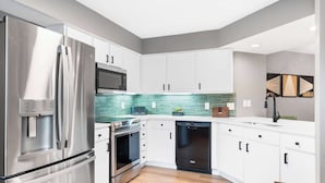 Une cuisine moderne dotée d’appareils électroménagers en acier inoxydable, de meubles blancs et d’un revêtement mural vert.