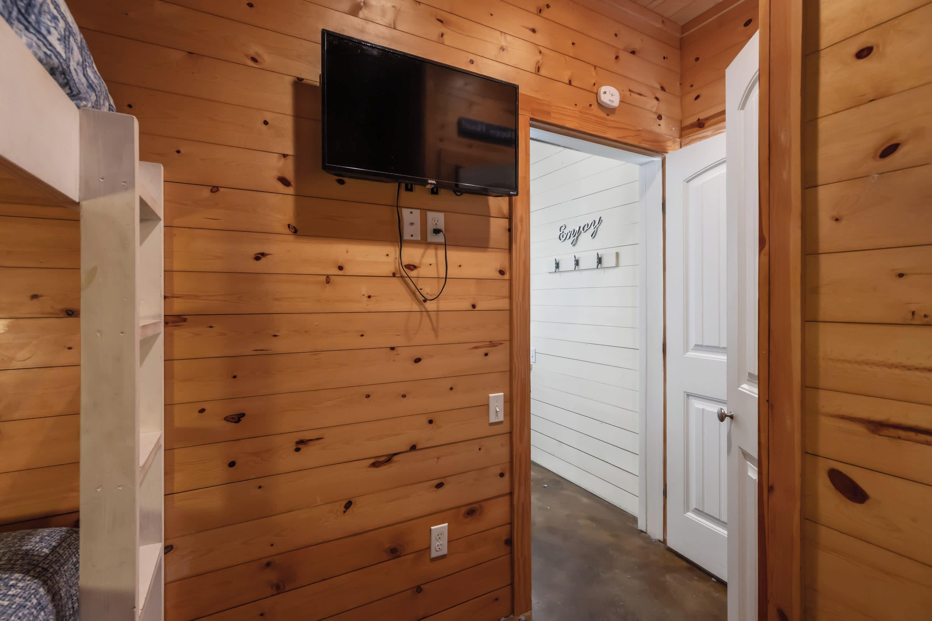 A wooden-paneled room with a mounted TV, a white door, and a wall-mounted thermostat.
