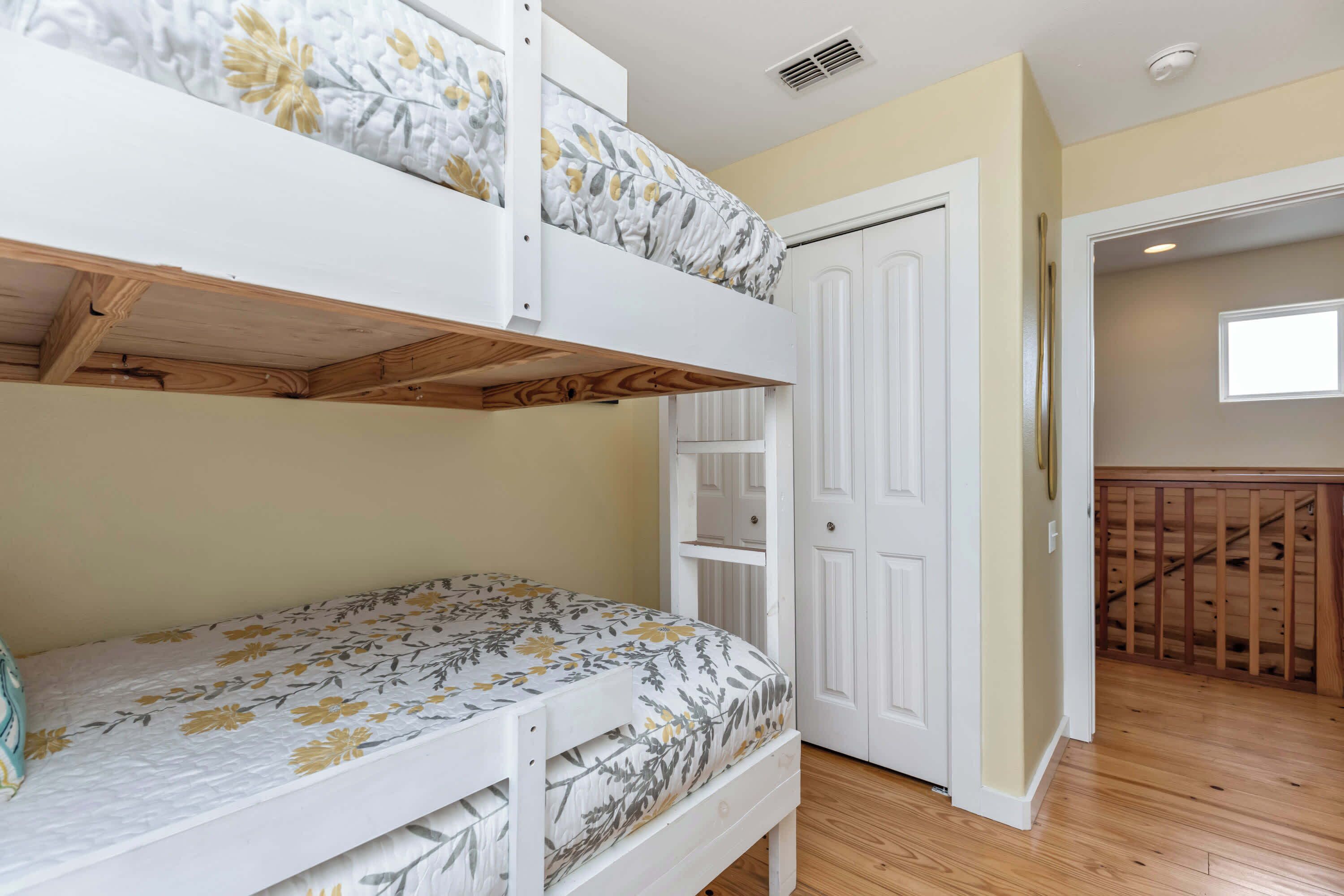 A bunk bed room with a wooden floor, a white door, and a window.