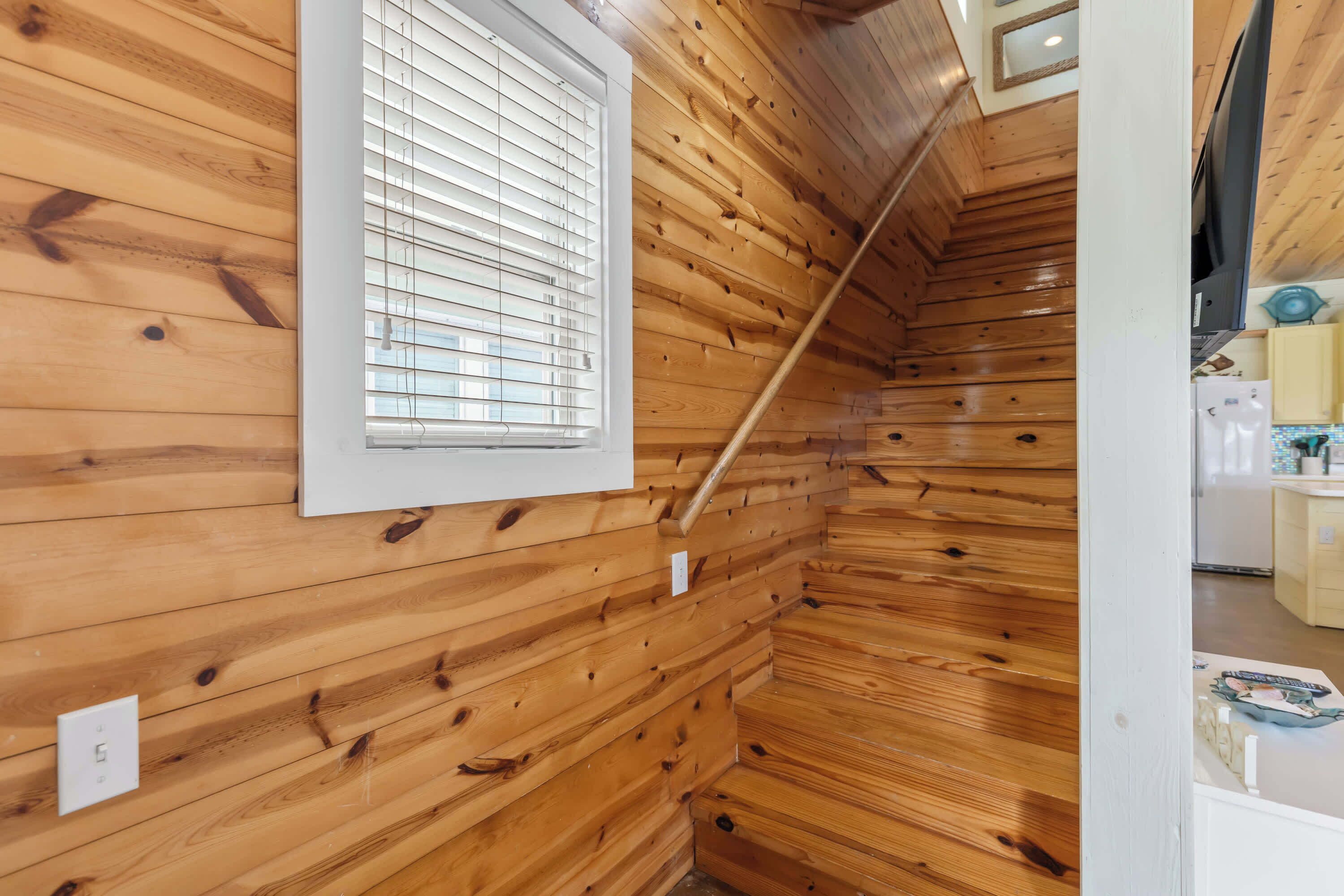 A wooden interior with a window, a wooden staircase, and a kitchen area with cabinets and appliances.