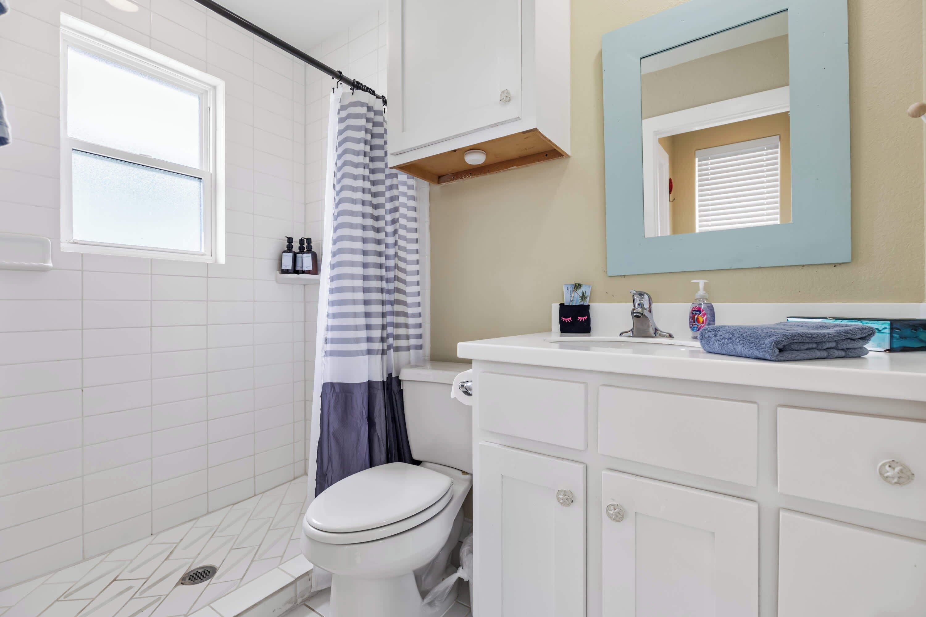 Une salle de bain avec des toilettes, une douche dotée d’un rideau à rayures, un lavabo avec un miroir et des articles de toilette posés sur le comptoir.