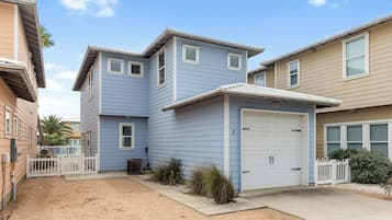 A two-story residential building with a garage, a fenced yard, and a clear sky.