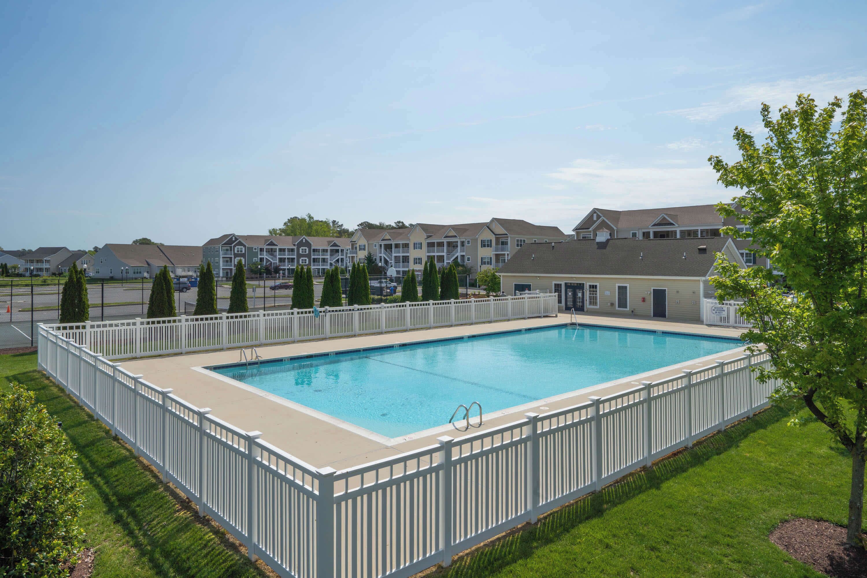 A rectangular swimming pool surrounded by a white fence, with a clear blue sky above.