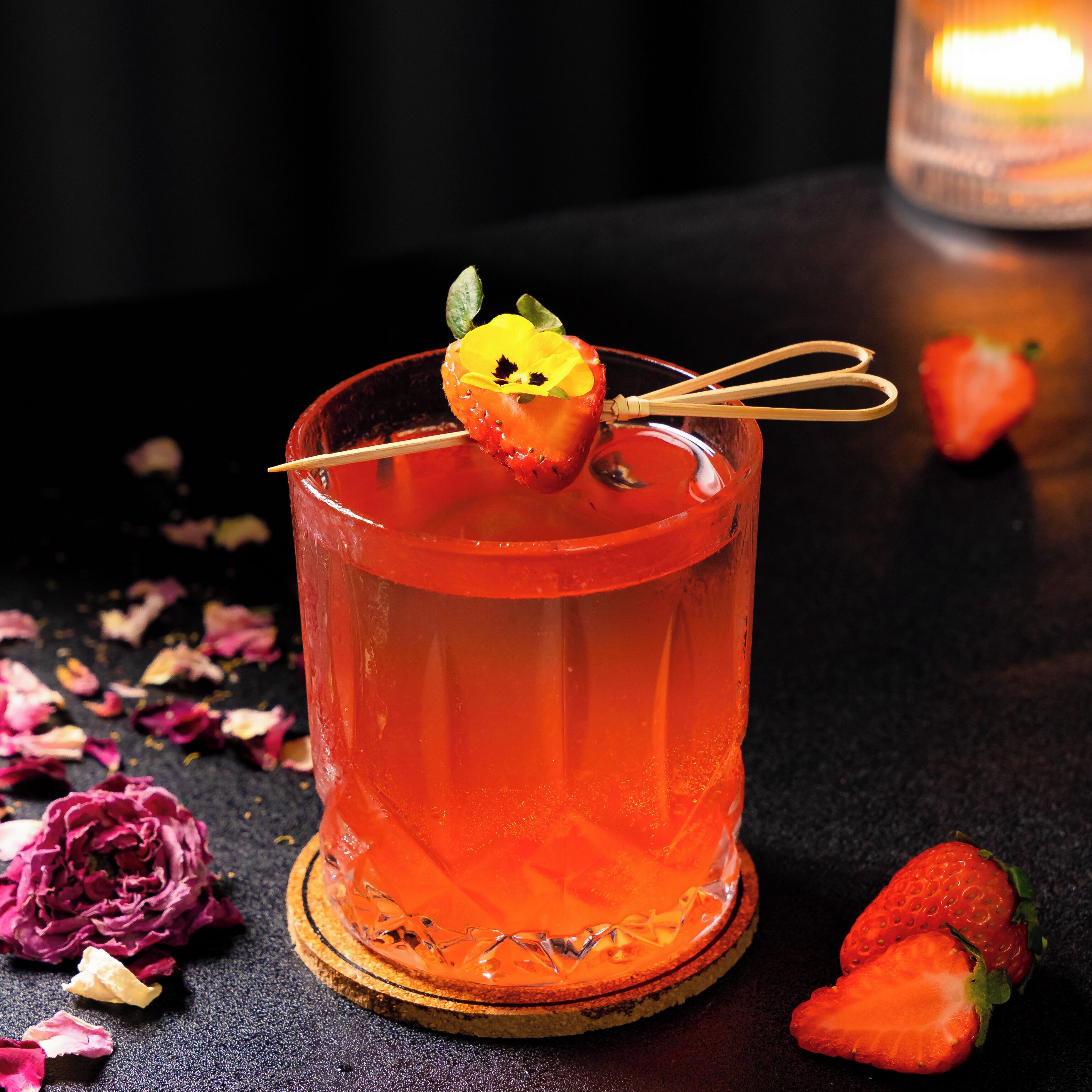 A cocktail glass with a strawberry garnish on a coaster.