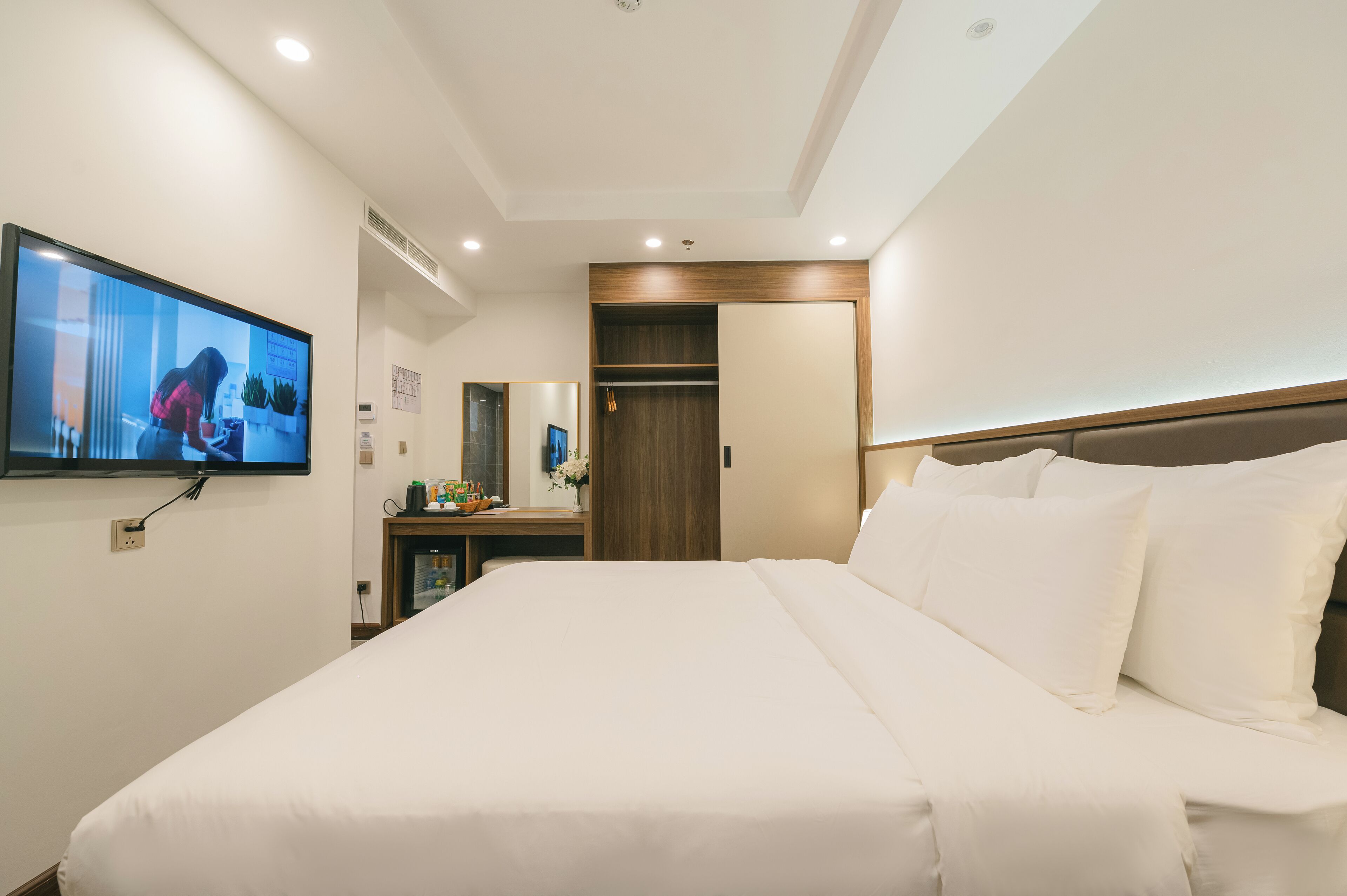 A hotel room with a large bed, a television mounted on the wall, a wooden wardrobe, and a mirror.