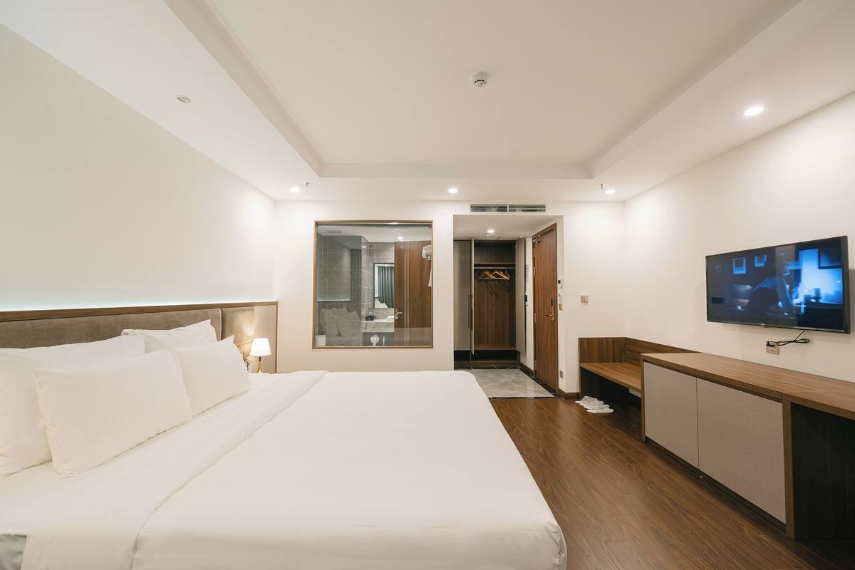 A modern hotel room with a large bed, a TV mounted on the wall, and a wooden desk.