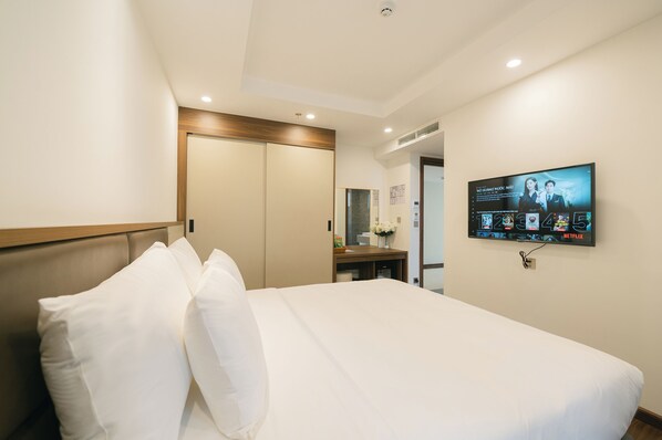 A hotel room with a bed, a TV mounted on the wall, and a wooden headboard.