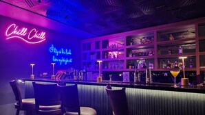 A bar area with neon signs, bar stools, and shelves stocked with bottles. - Love St Hotel (Hanoi)