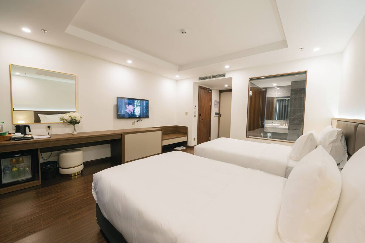 A modern hotel room with two beds, a TV, a minibar, and a bathroom mirror.