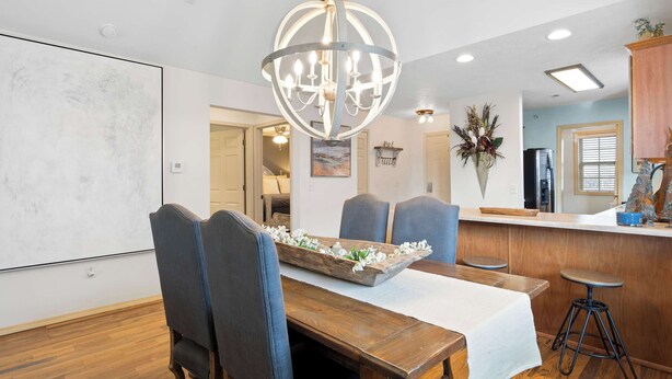 Uma sala de jantar com uma mesa de madeira, cadeiras estofadas em azul, um lustre e um espaço bar com bancos.