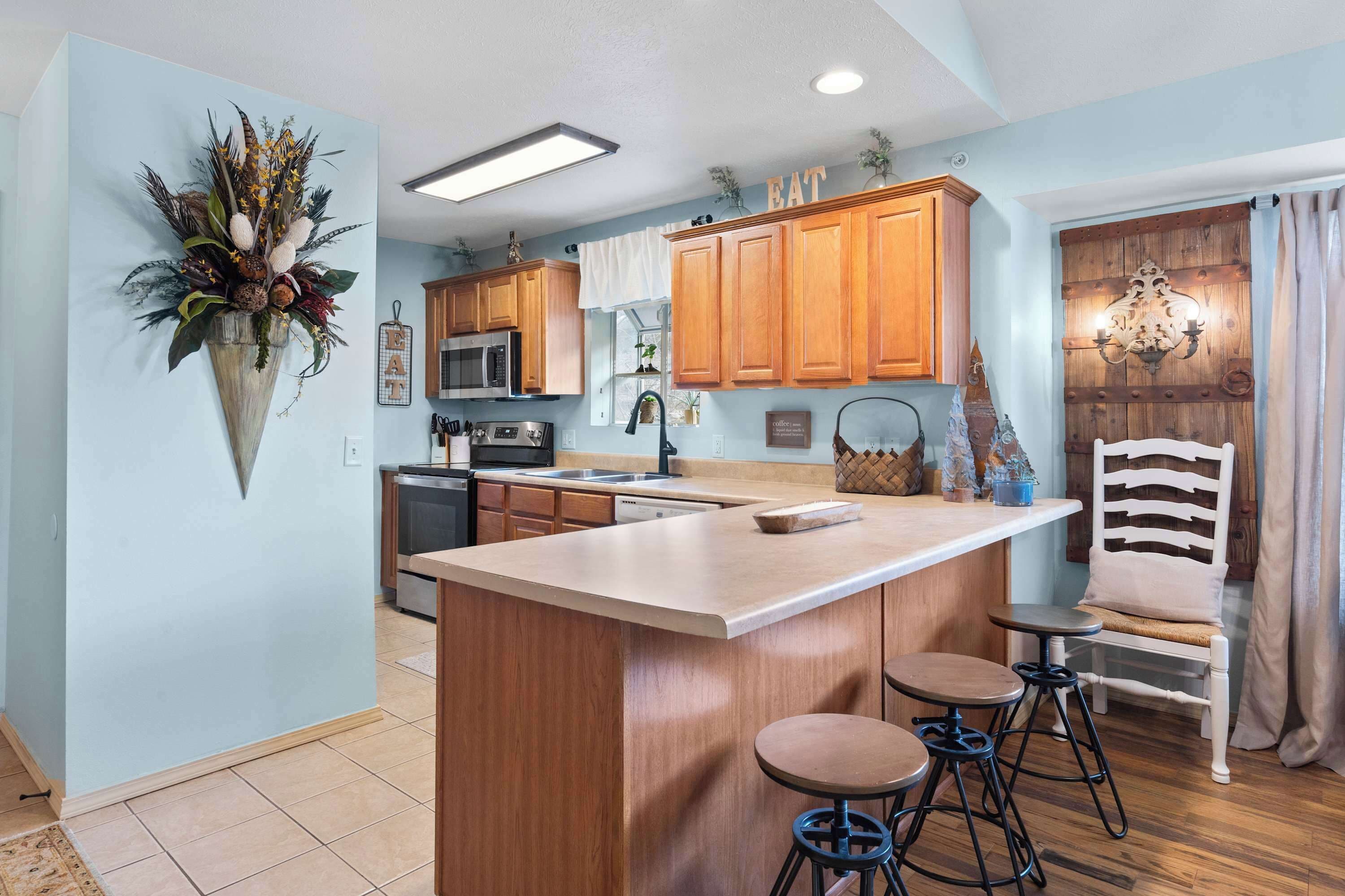 A kitchen with wooden cabinets, a central island with stools, a hanging plant, and a chandelier.